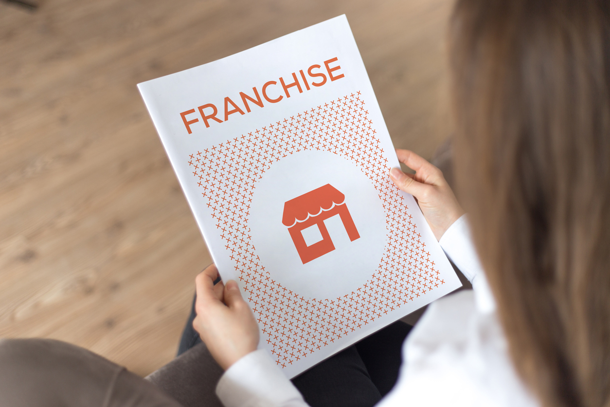 Person holding a brochure titled "FRANCHISE" featuring an icon of a storefront, symbolizing local SEO strategies for franchise success.