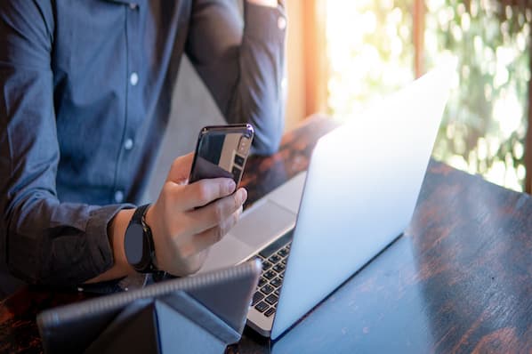 Person using smartphone and laptop at a desk, illustrating digital communication and networking strategies for LinkedIn messaging.